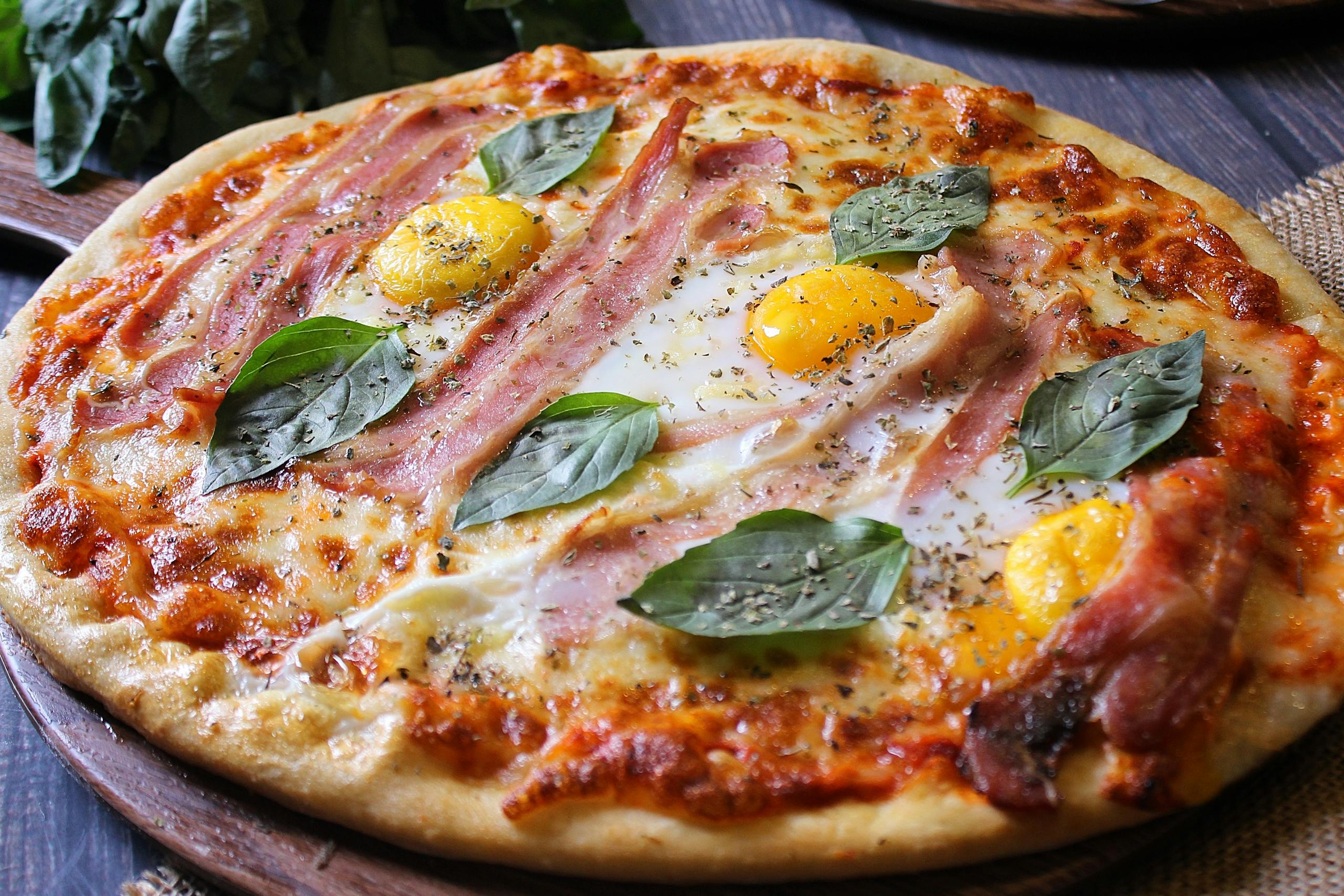 Tejfölös extra pizza 1 Delicious gourmet pizza topped with ham, eggs, and fresh basil leaves, perfect for a culinary delight.